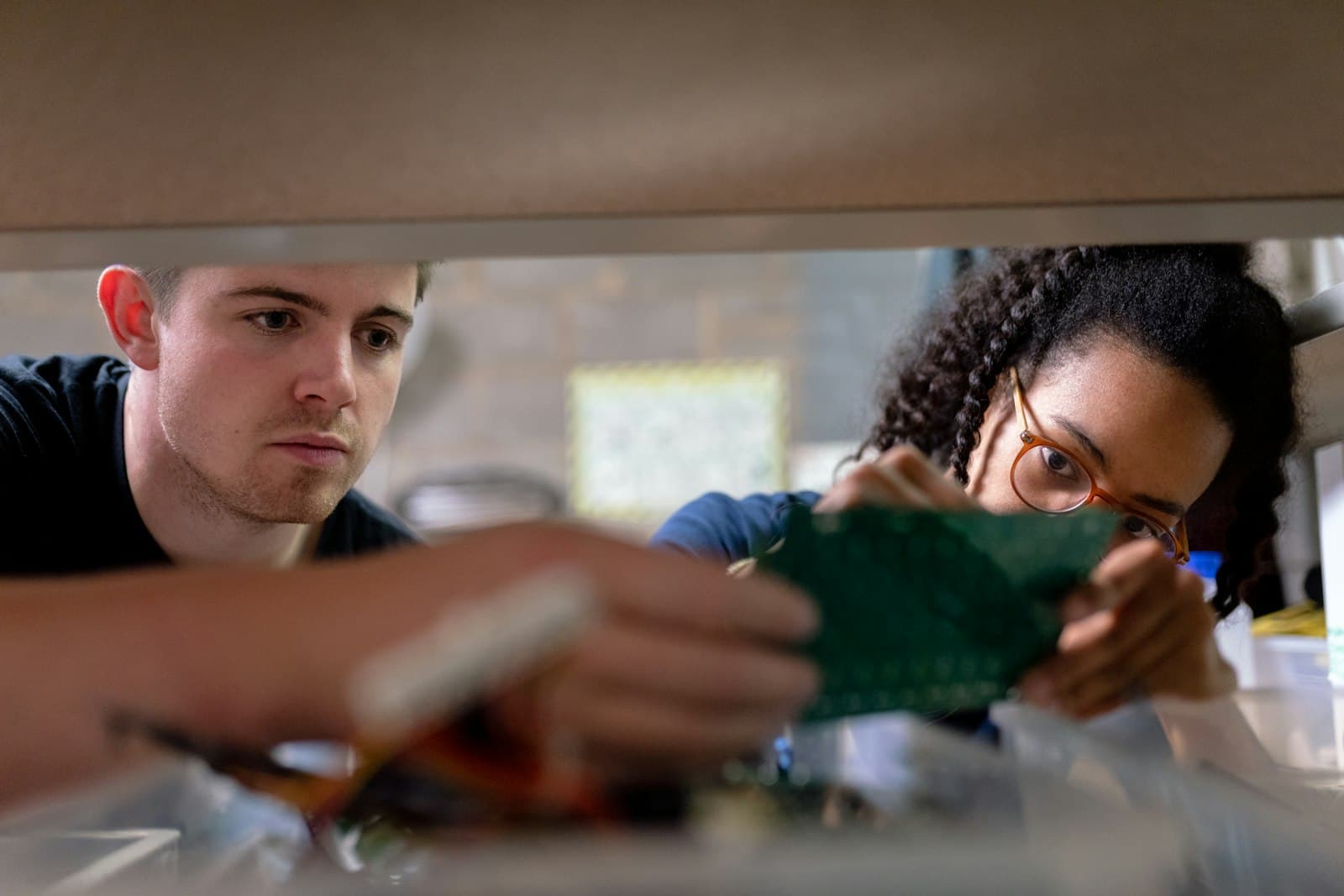 Two people examining a green circuit board they are working on in a workshop.